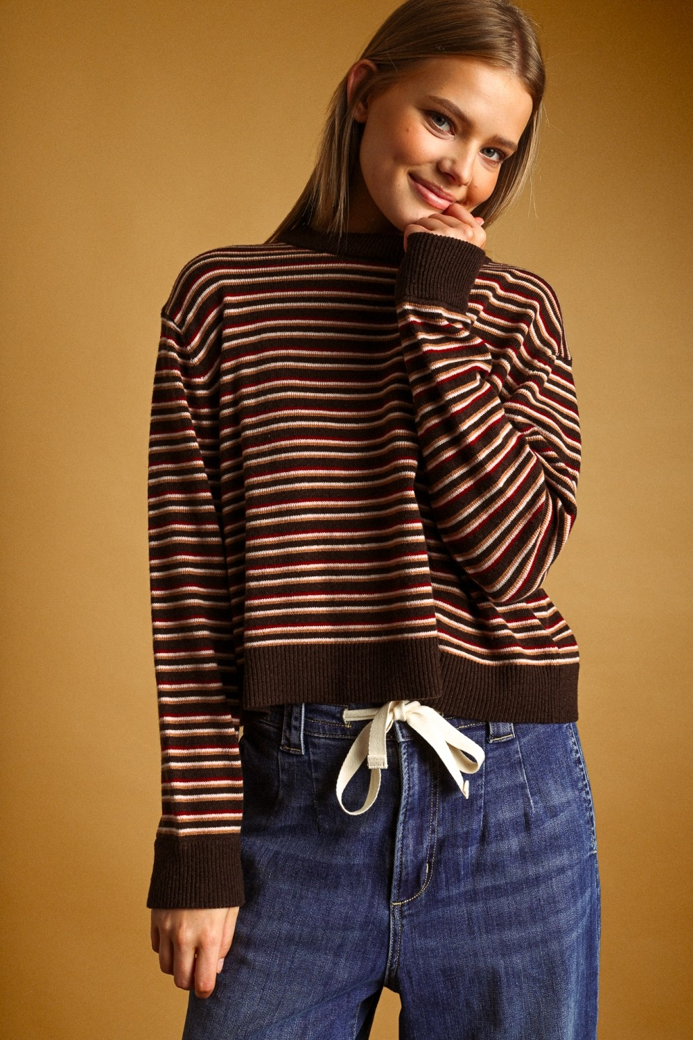 Woman wearing a Carol multi-color striped round neck knit top with high-waisted denim jeans.