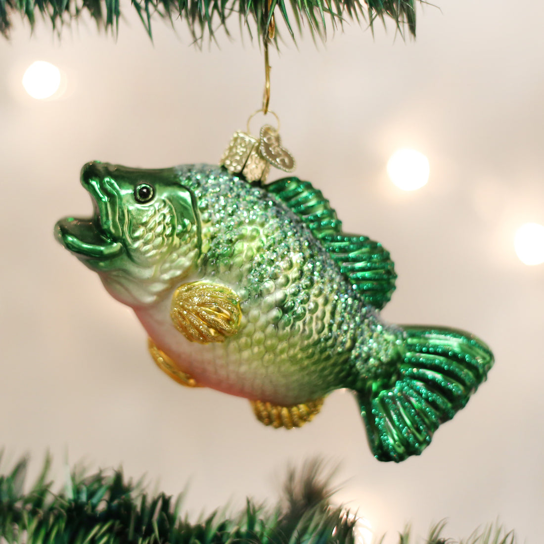 Green and gold glittery glass largemouth bass Christmas ornament hanging on a tree.