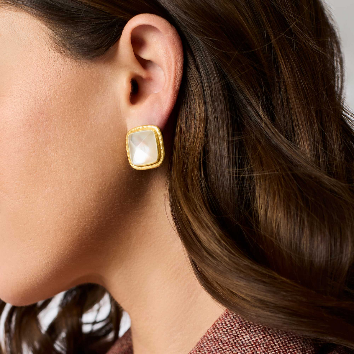 A woman wearing a Sahara Stone Stud earring featuring a square white glass stone in 24K gold plate.