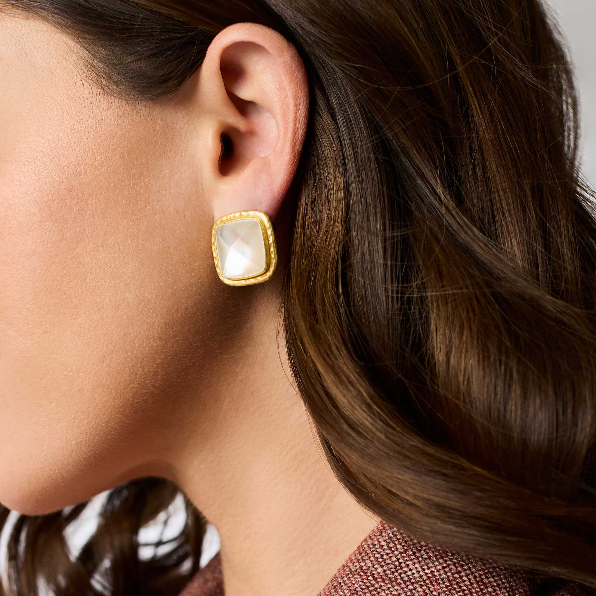 A woman wearing a Sahara Stone Stud earring featuring a square white glass stone in 24K gold plate.