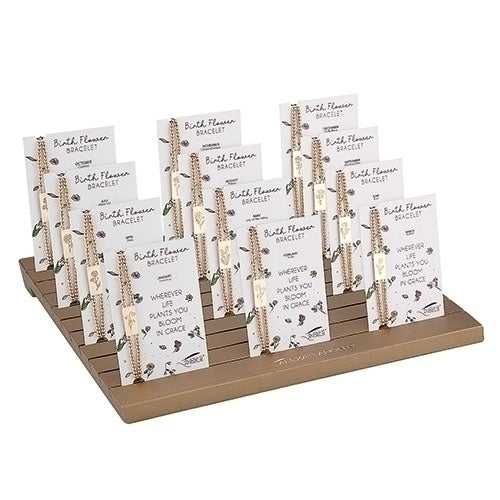 A wooden display stand holding several Birth Flower Bracelet cards with gold chain bracelets.