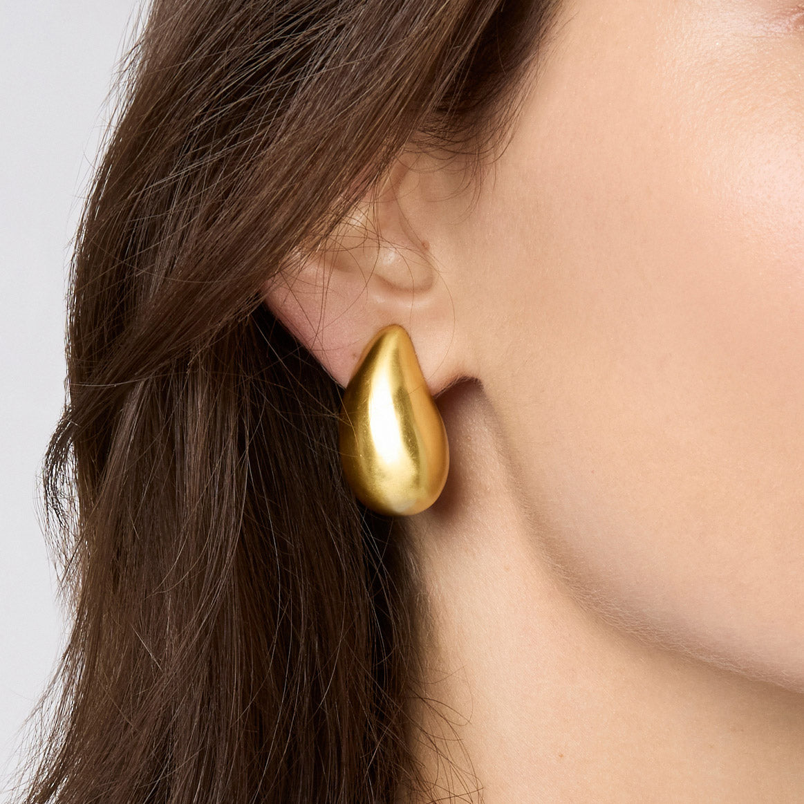 A person wearing a smooth, teardrop-shaped Wave Clip earring in 24K gold plate.