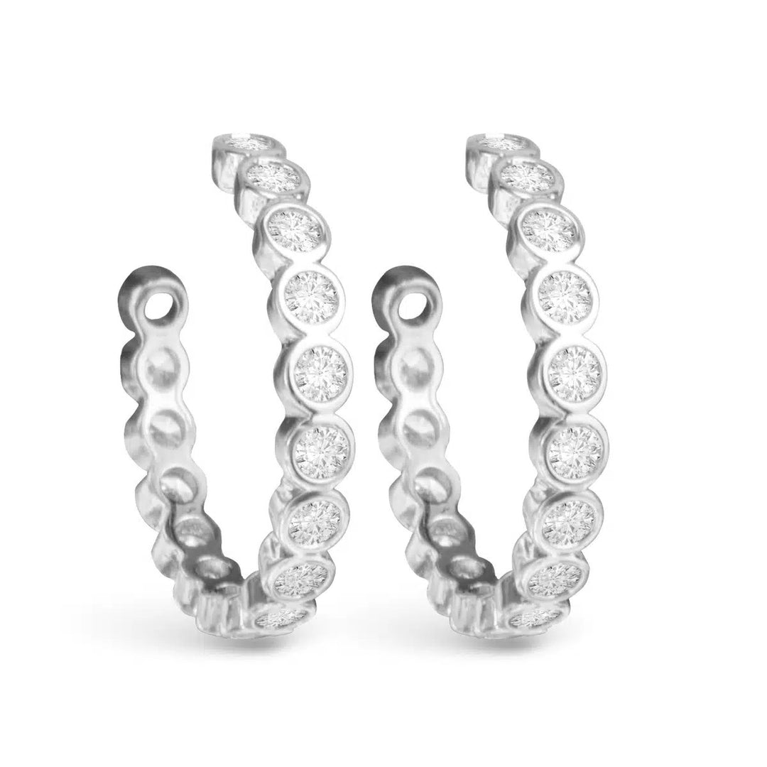 Pair of silver hoop earrings featuring round bezel-set cubic zirconia stones.