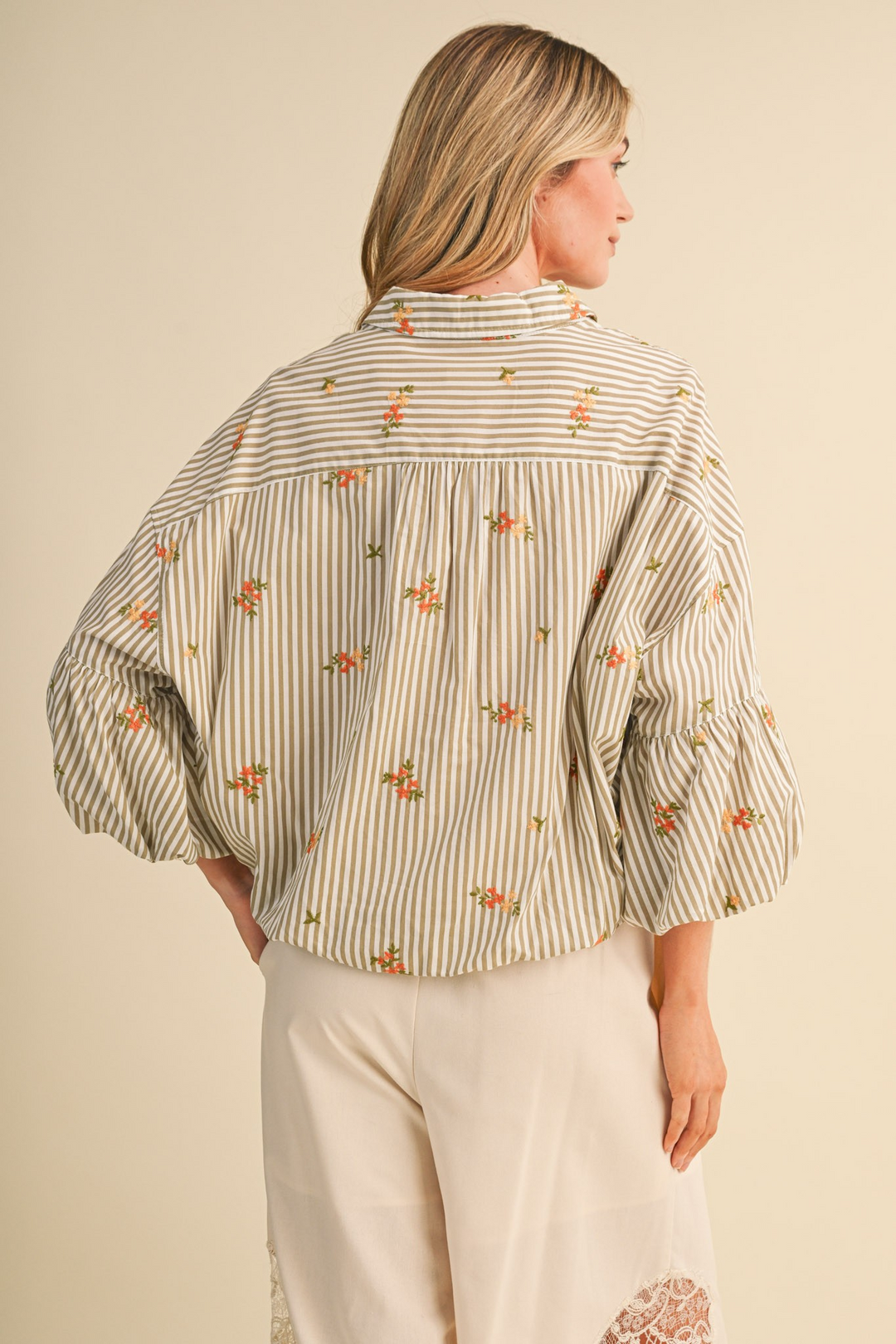 Back view of a woman wearing a striped button-down top with floral embroidery and bubble sleeves.