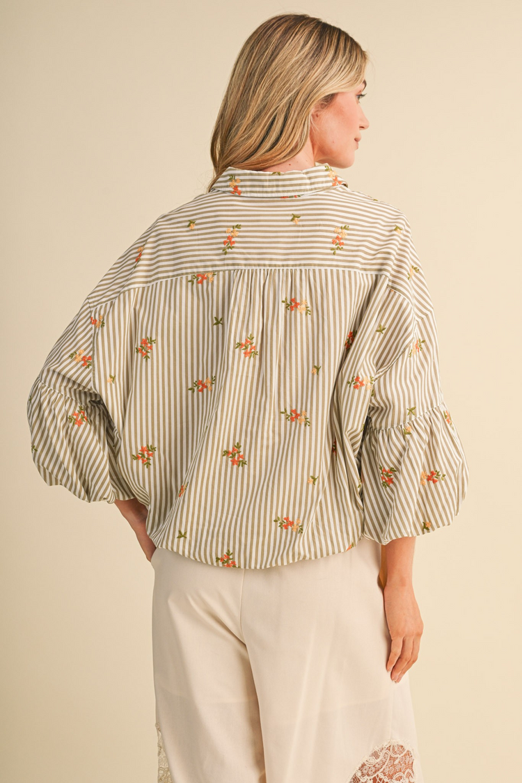 Back view of a woman wearing a striped button-down top with floral embroidery and bubble sleeves.