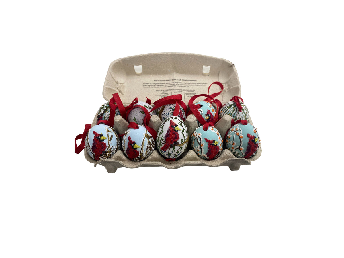 Ten cardinal egg ornaments with red ribbons displayed in a cardboard egg carton.
