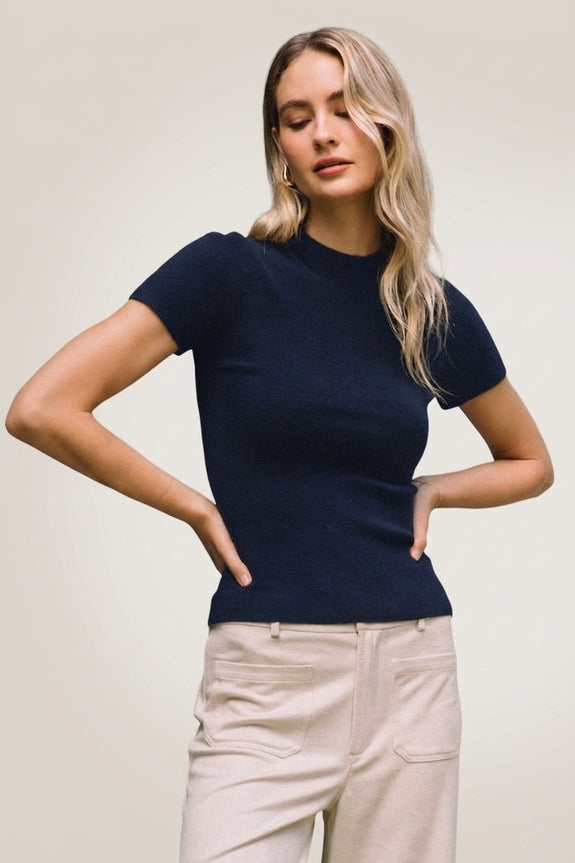 Woman wearing a navy blue Lucy short sleeve mock neck soft knit sweater top with beige trousers.