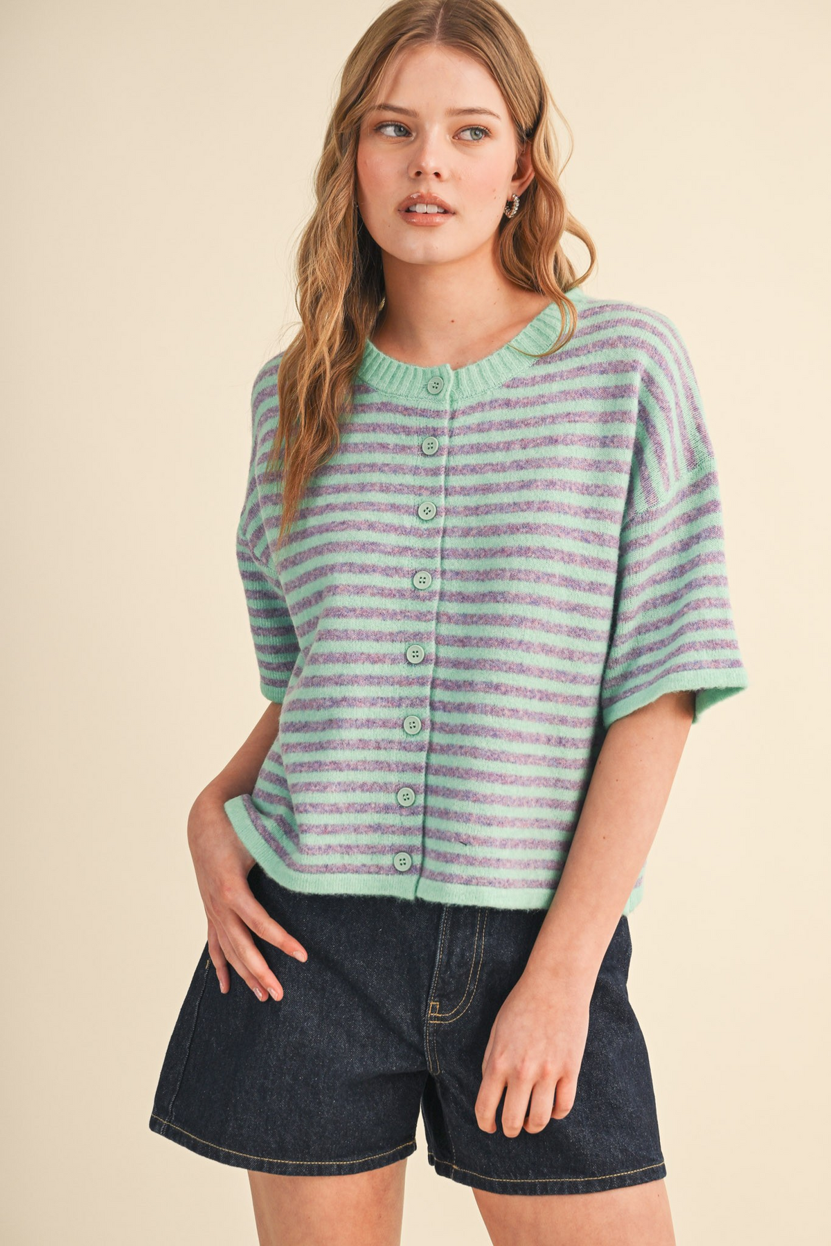 Woman wearing the Ivy Striped Short Sleeve Sweater Cardigan in mint and purple with denim shorts.