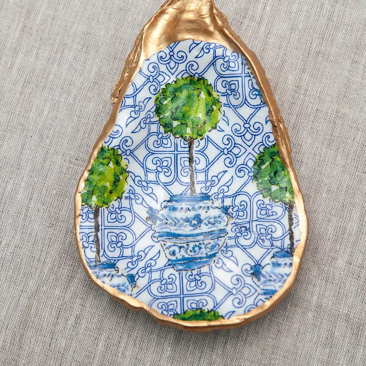 Decoupaged oyster shell with blue and white patterns, a green topiary, and gold metallic trim.