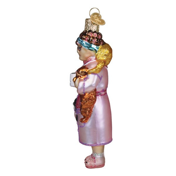 Side view of a glass Cat Lady Ornament wearing a pink robe and holding a cat and a mug.