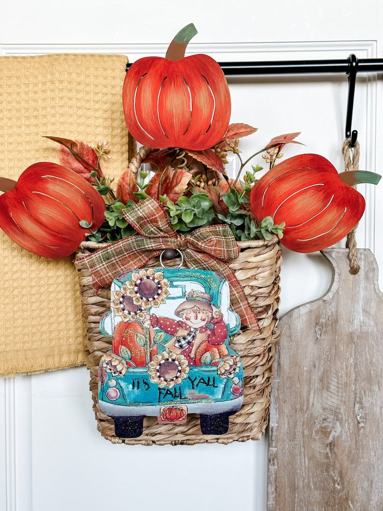 Three orange metal pumpkin stakes with green stems arranged in a decorative woven basket.