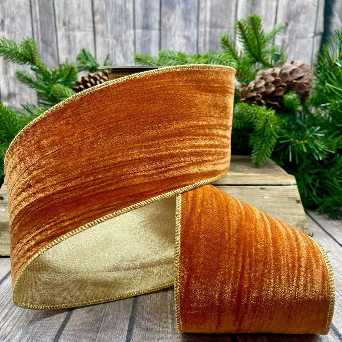 4 inch wide persimmon velvet ribbon with gold backing and wired edges on a wooden surface.