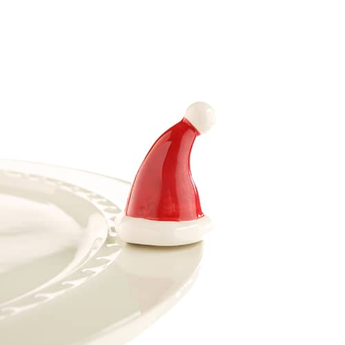 Miniature Santa hat ornament with white trim and pom-pom, resting on the edge of a white plate.