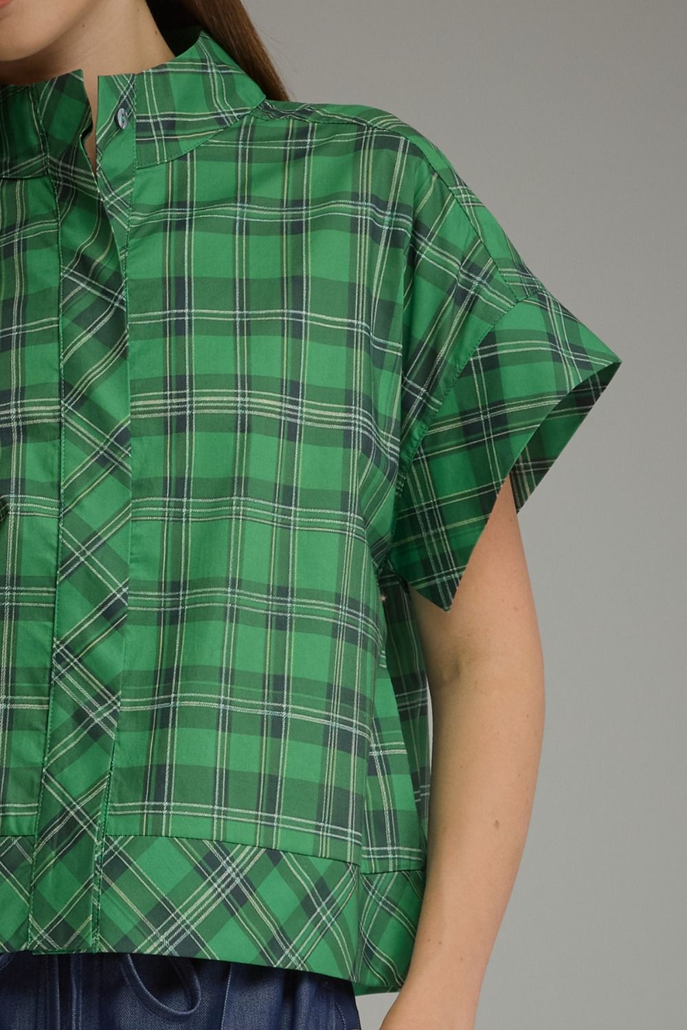 Close-up of a green plaid short sleeve top with a button-up collar and wide sleeves.
