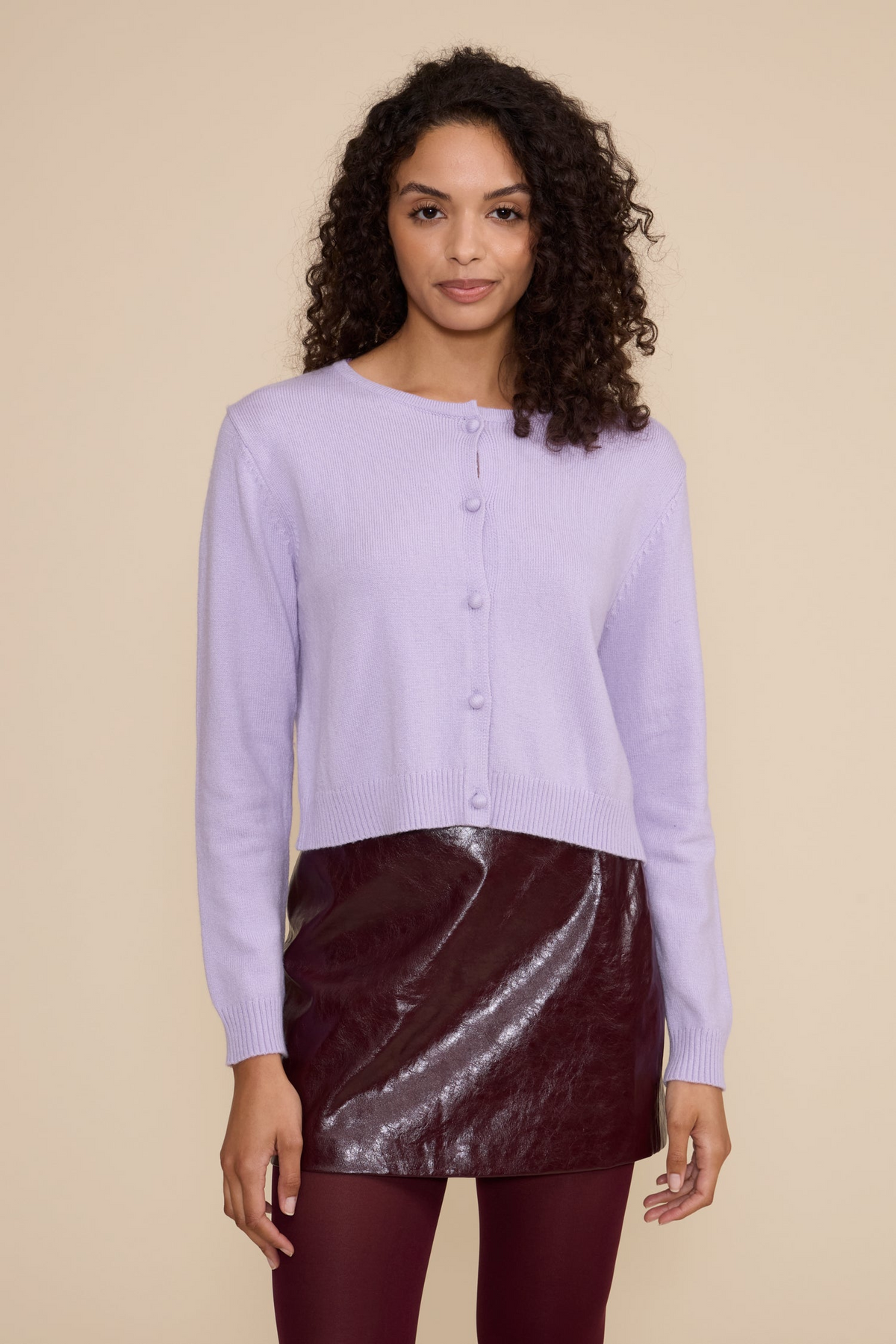Woman wearing a lavender Lucy Judd cropped cardigan with a burgundy patent leather skirt.