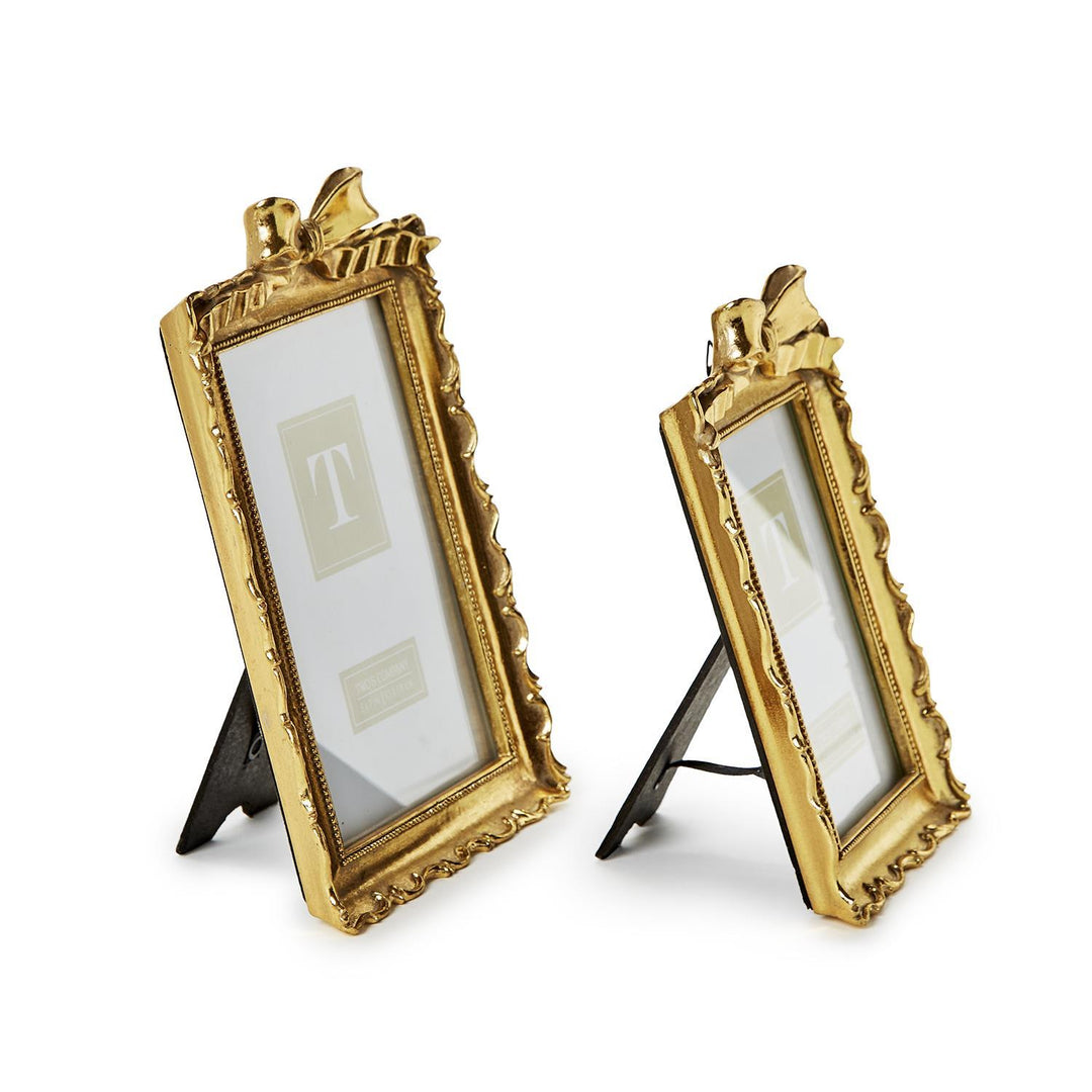 Two vintage-style gold resin picture frames with decorative bows on top, standing on a white surface