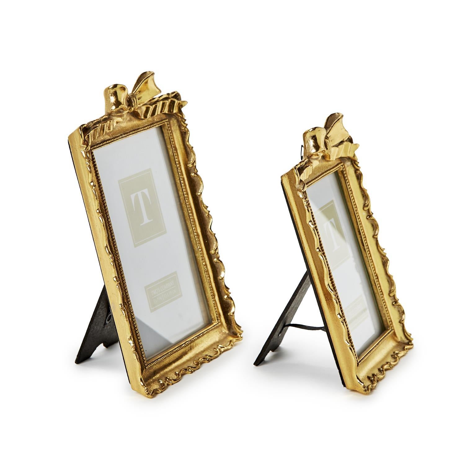 Two vintage-style gold resin picture frames with decorative bows on top, standing on a white surface