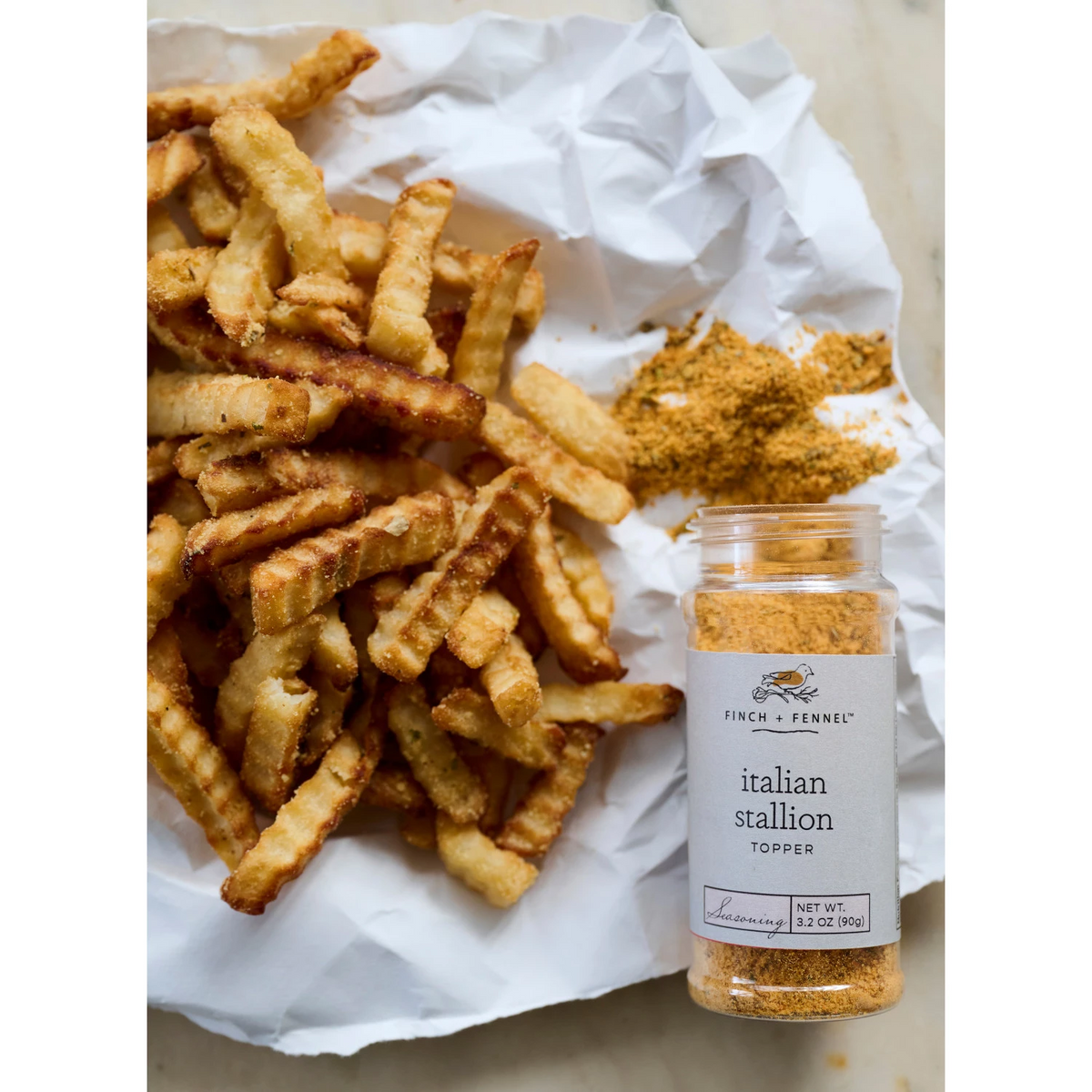 A jar of Italian Stallion Topper Seasoning next to seasoned crinkle-cut french fries.