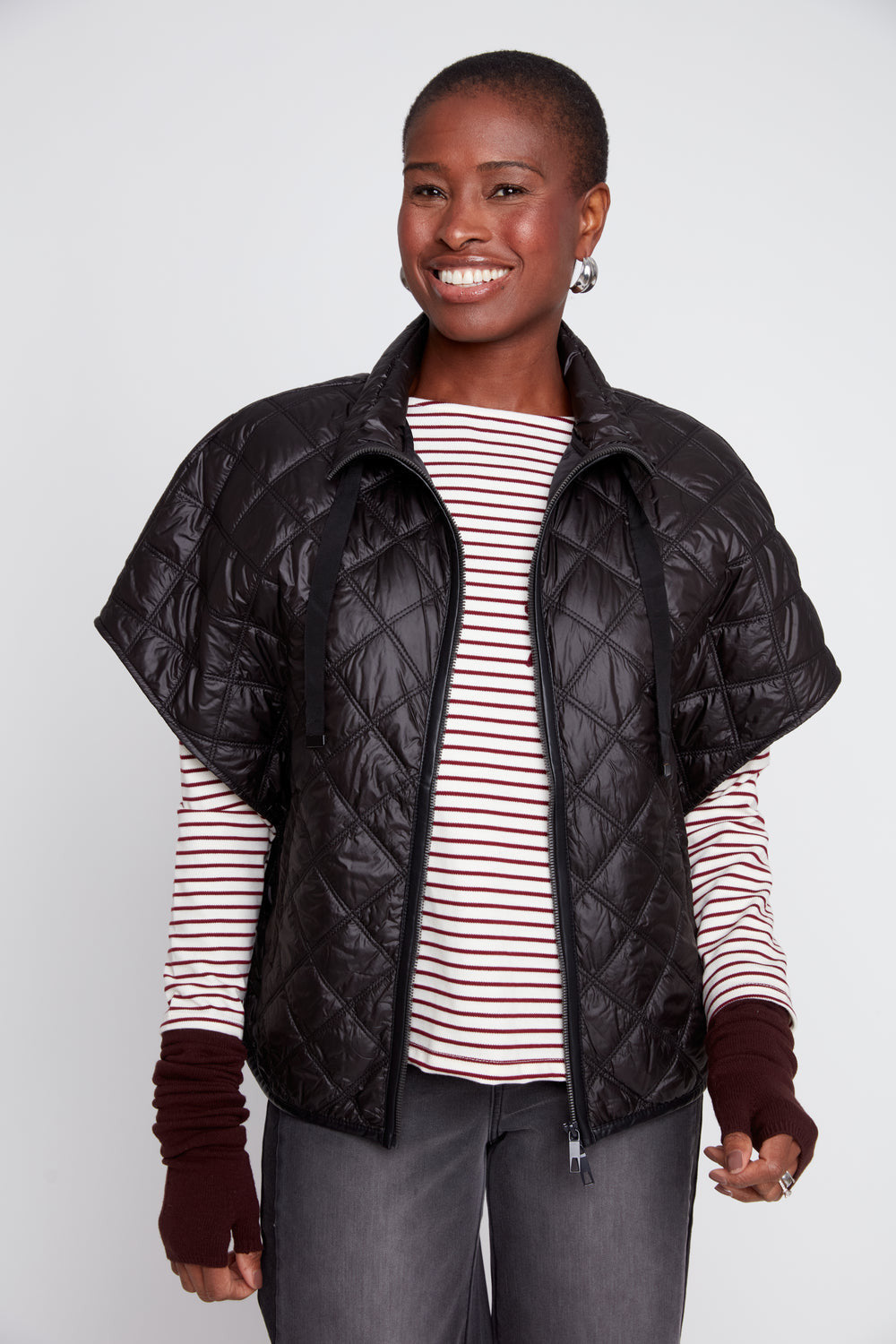 A woman wearing the Megan Luxe Quilted Poncho in black over a striped long-sleeve shirt.