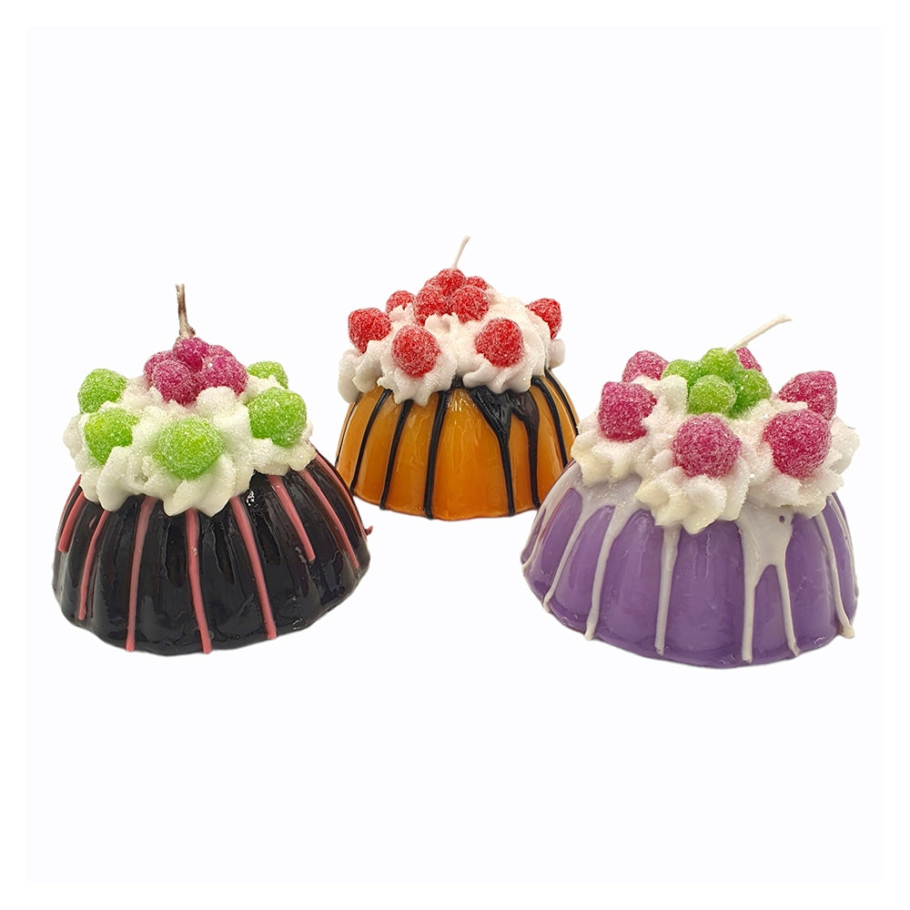 Three little pudding shaped candles in black, orange, and purple with whipped wax and berry tops.