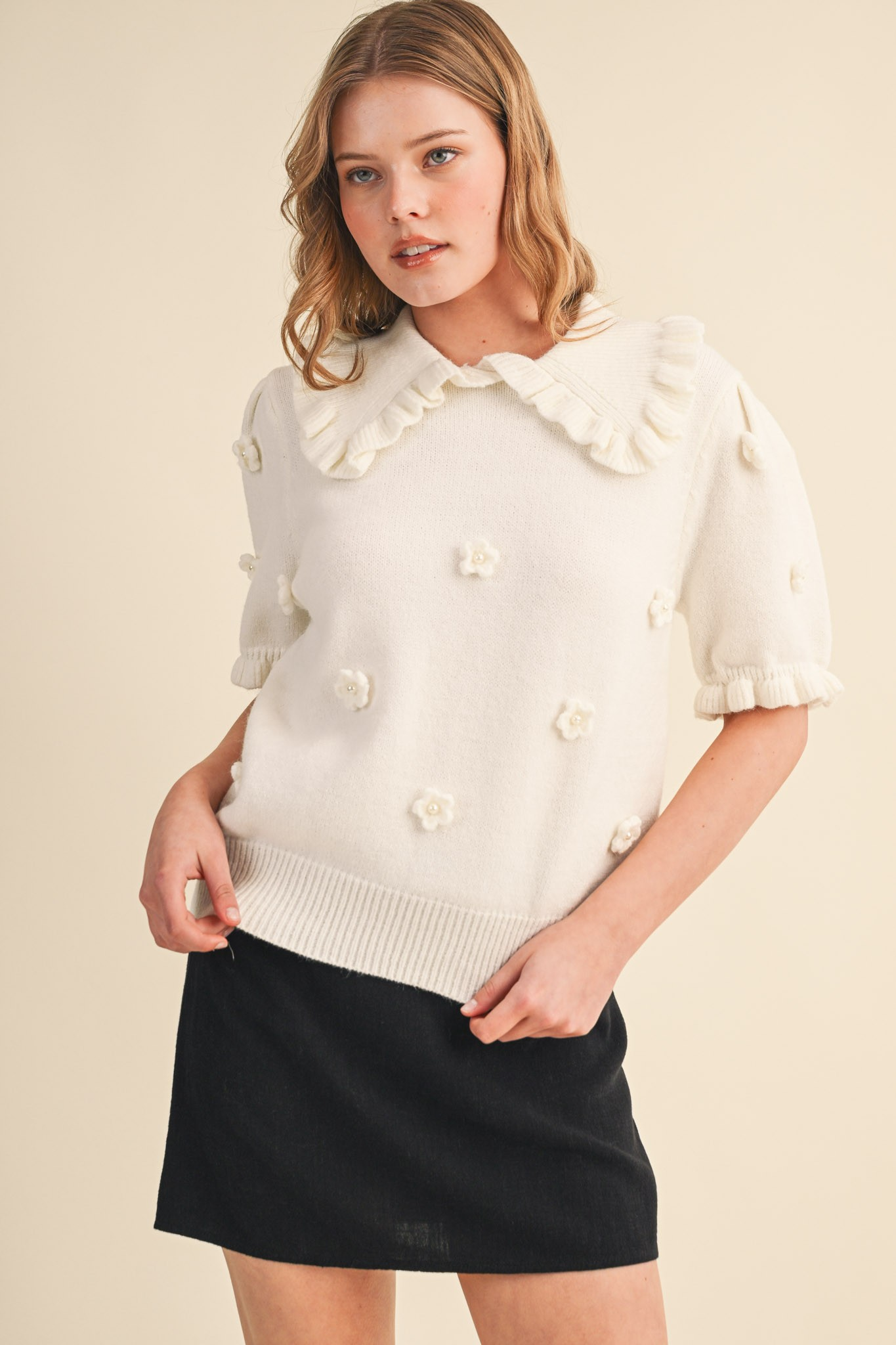 Woman wearing a white short-sleeve sweater with floral pearl appliqué and a ruffled doll collar.