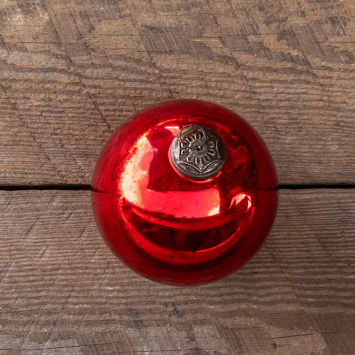Extra large antique shiny ruby glass ball ornament on a rustic wooden surface.