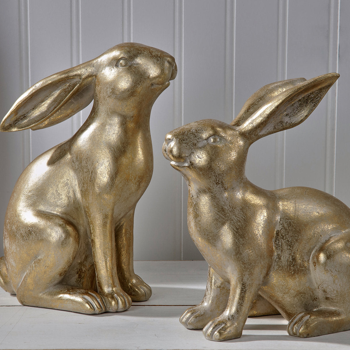 Two golden resin bunny figurines with a distressed finish sitting on a white surface.