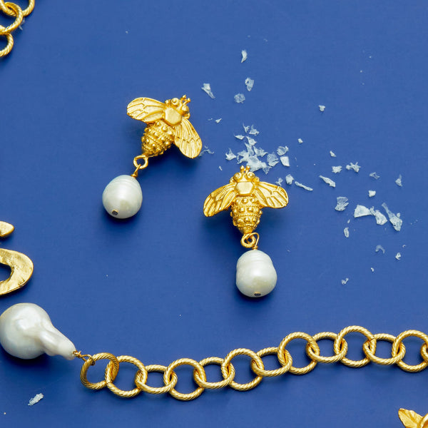 Gold bee earrings with genuine freshwater pearl drops on a blue background.