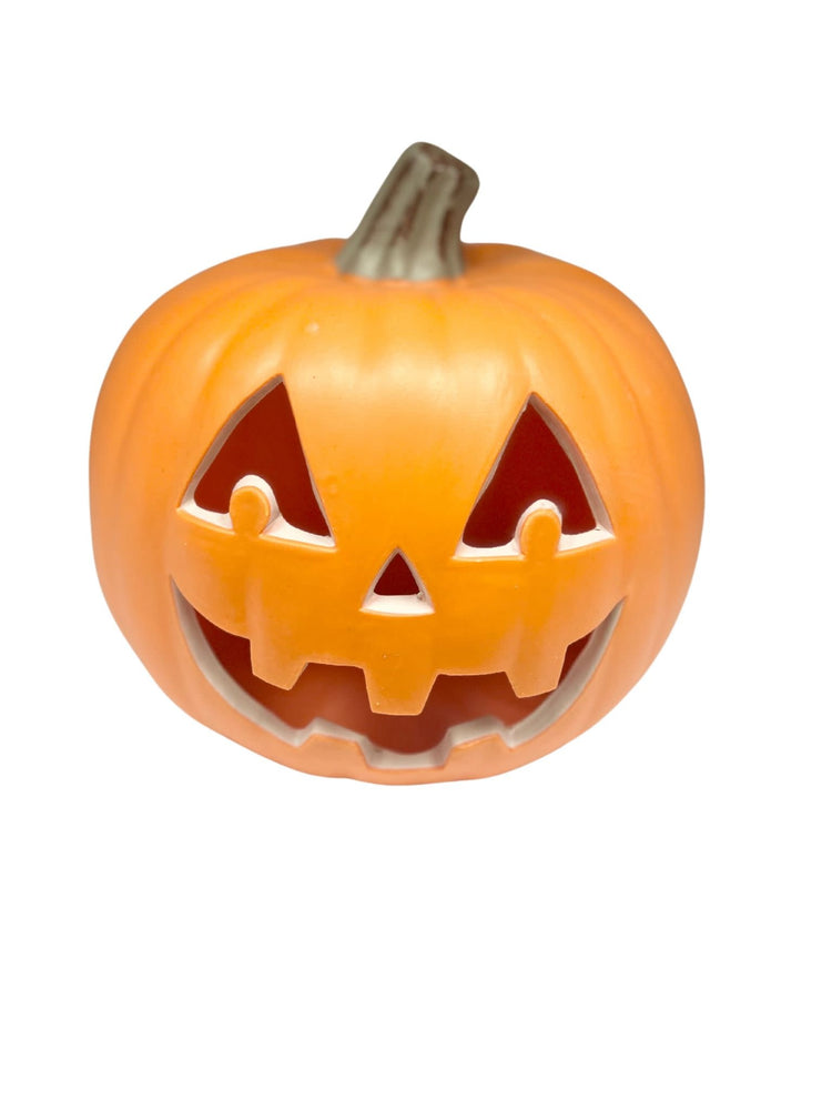 Small lighted pumpkin with a carved jack-o'-lantern face glowing in orange.
