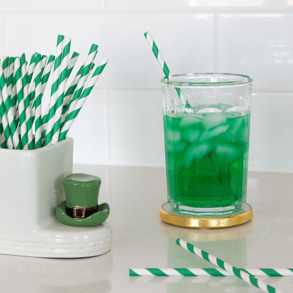 Green and white striped paper straws in a white holder next to a green drink with a leprechaun hat decoration.