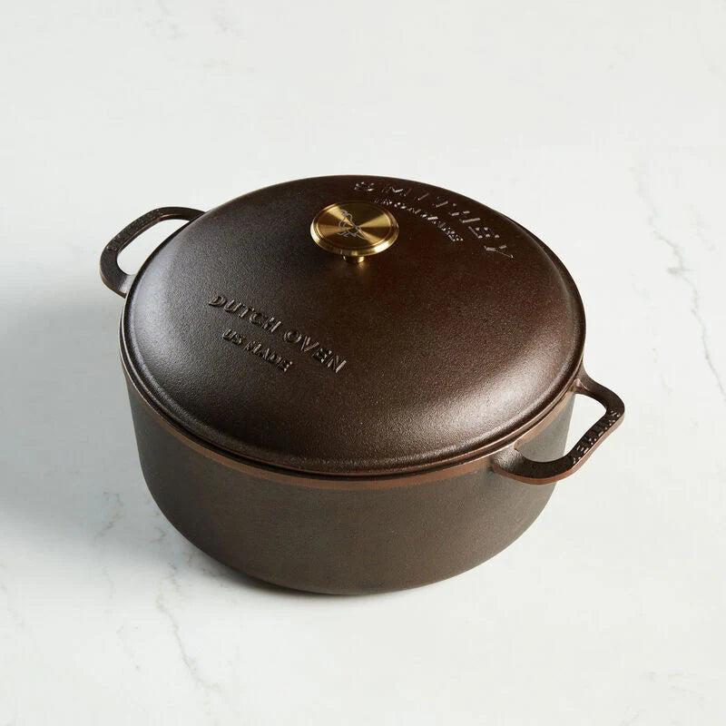 Smithey 7.25 QT cast iron Dutch oven with domed lid and gold-toned knob on a white marble surface.