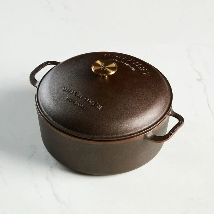 Smithey 7.25 QT cast iron Dutch oven with domed lid and gold-toned knob on a white marble surface.