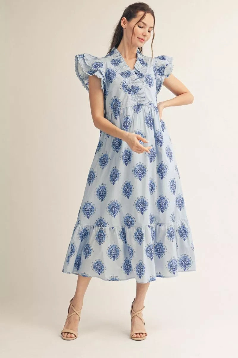 Woman wearing a light blue floral midi dress with ruffled cap sleeves and a tiered hem.