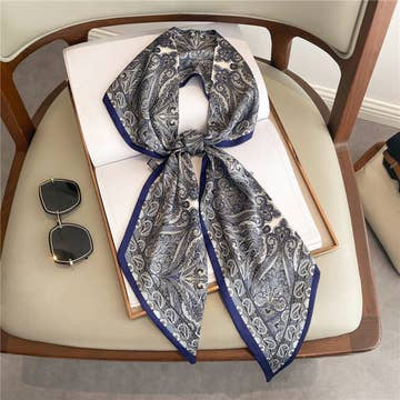 Blue and white paisley print double-layer head scarf tied in a bow on a chair next to sunglasses.
