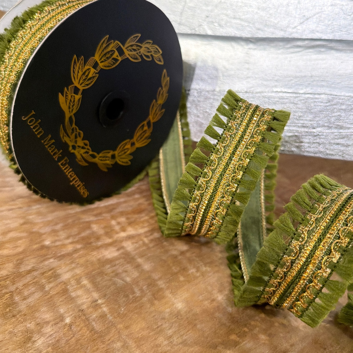 1.5 inch green dupion ribbon with gold embroidery and double tassel fringe on a black spool.