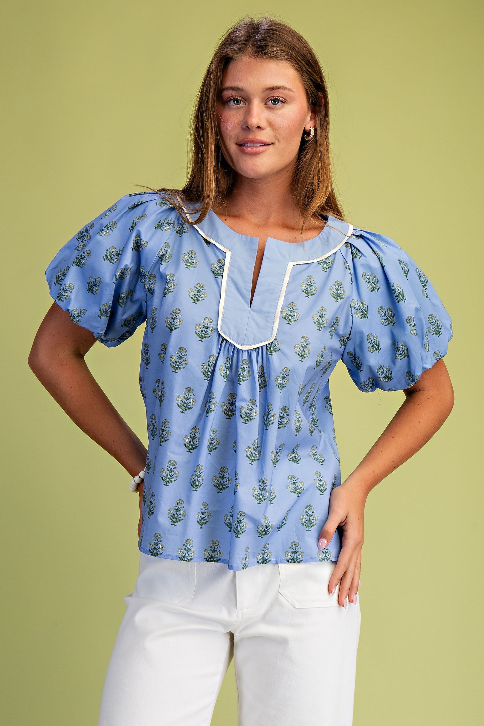 Woman wearing a blue Hannah floral printed notch neck pleated blouse with short puff sleeves.