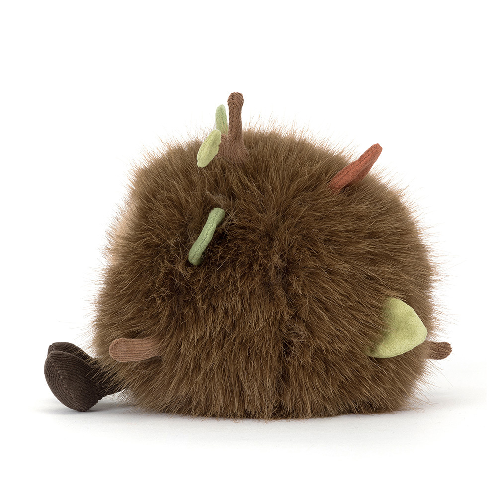 Round, fuzzy brown plush toy with small green leaves and brown twigs sticking out of its fur.