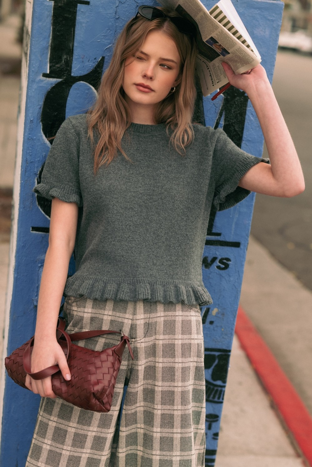 Woman in a charcoal Helena ruffle hem short sleeve sweater top and plaid wide-leg trousers.