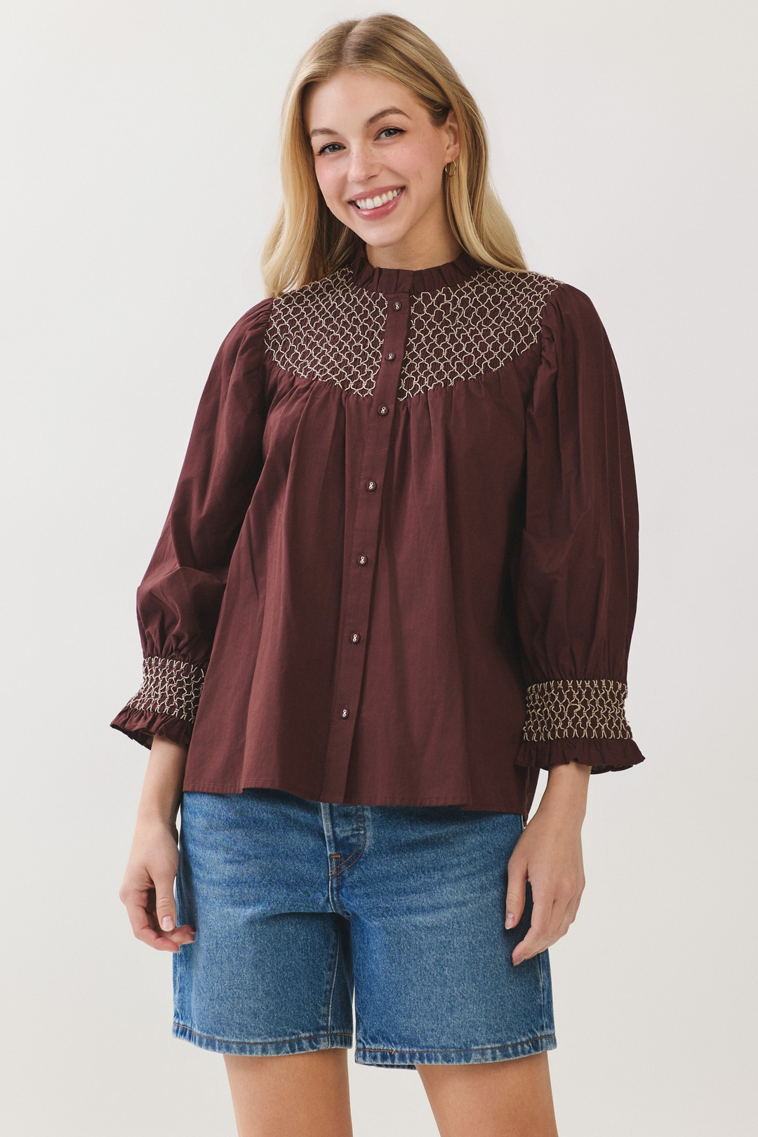 Woman wearing a Jenny Embroidered Button Down Blouse in burgundy with blue denim shorts.