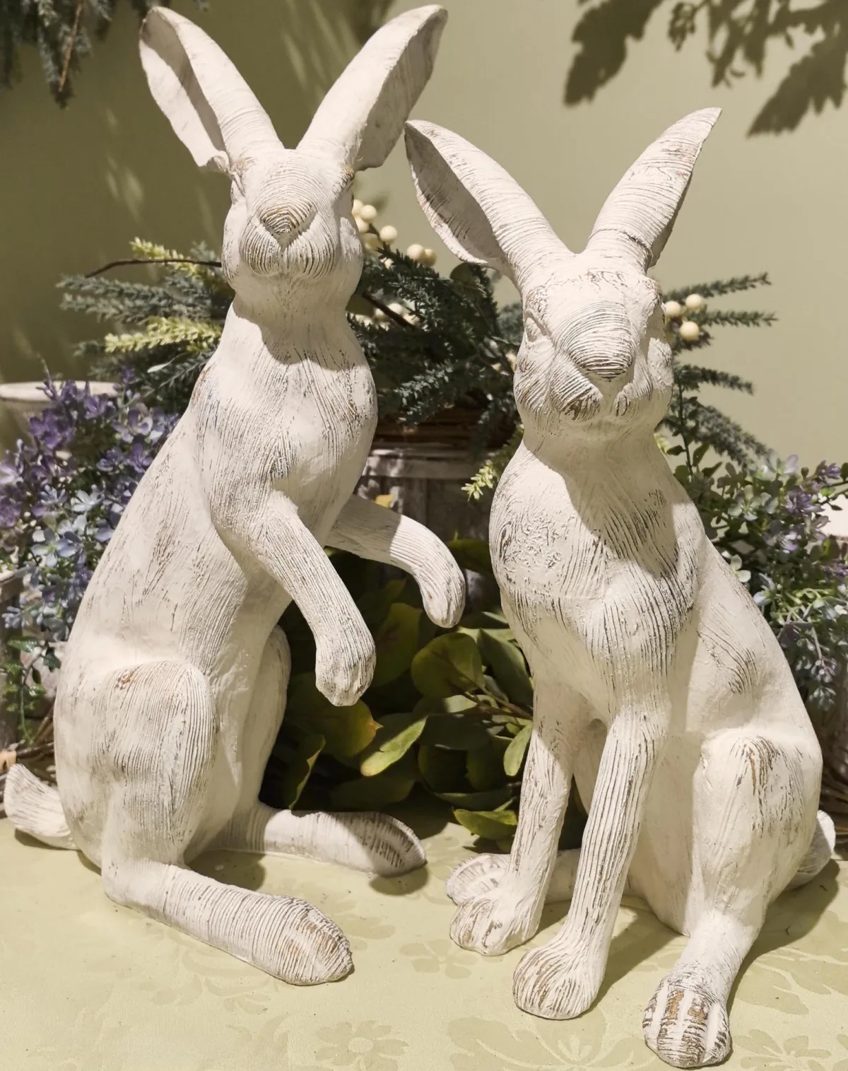 Two distressed white wooden bunny statues with long ears, one sitting and one in a half-sitting pose.