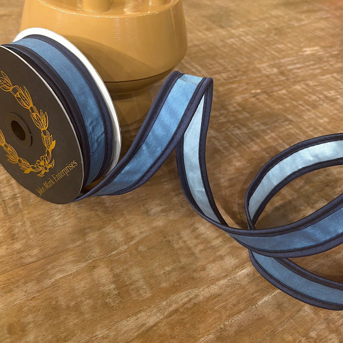1x10yd Blue and Royal Taffeta Double Piping Ribbon on a spool and unrolled on a wooden surface.