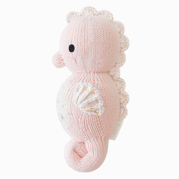 Hand-knit baby seahorse plush toy in powder pink with white scalloped details.
