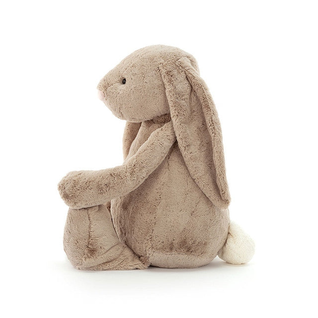 Side view of a gigantic bashful beige plush bunny with long floppy ears and a white fluffy tail.