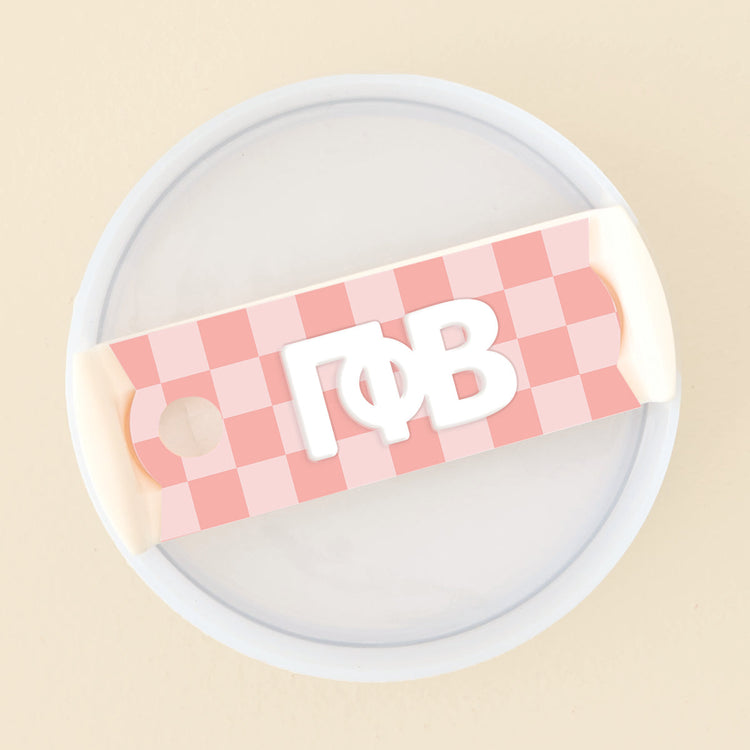 Pink checkered acrylic tumbler lid tag featuring white Greek letters Gamma Phi Beta.