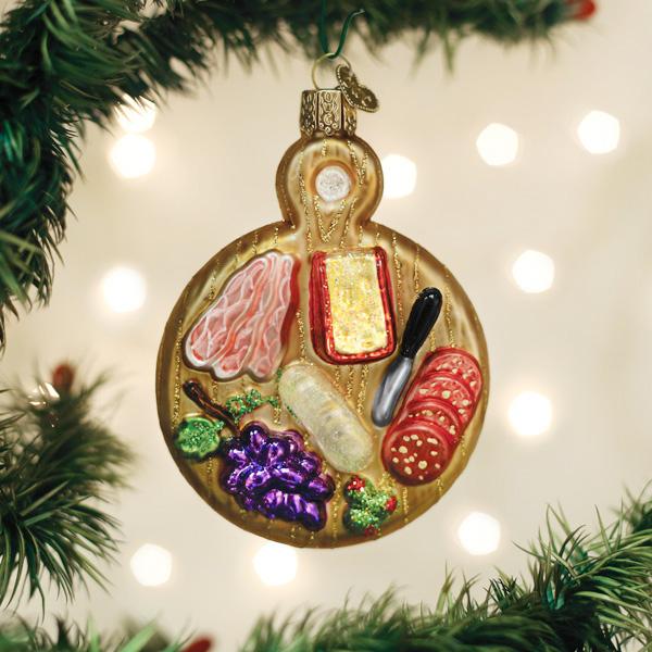 Glass charcuterie board ornament featuring cheese, meats, grapes, and a knife on a gold background.