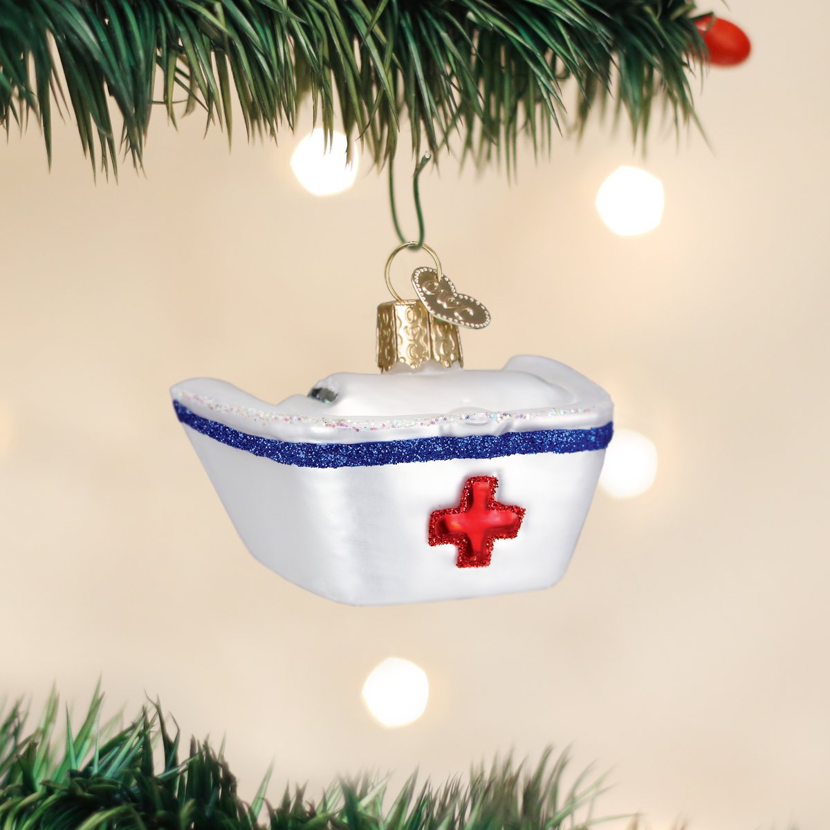 White glass nurse's cap Christmas ornament with a blue glitter band and red cross.