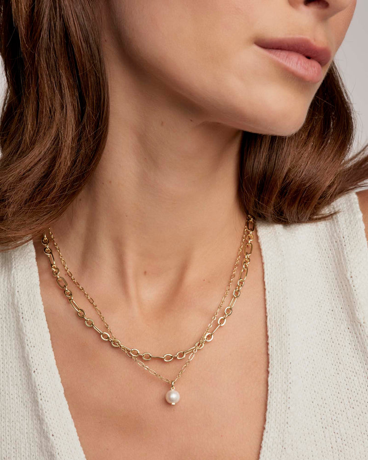 Close-up of a person wearing the Ashton Multi Strand gold chain necklace with a pearl pendant.