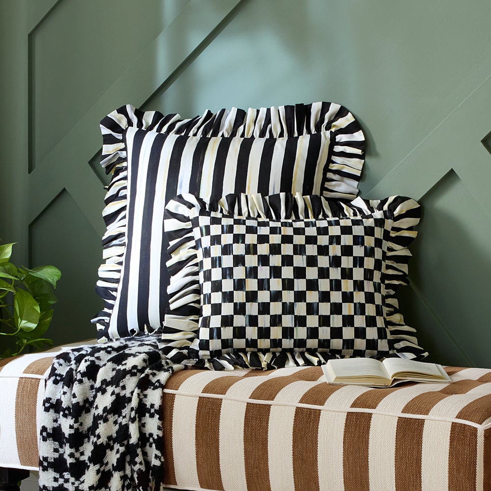 Black and white striped throw pillow with ruffled edges on a brown striped bench.