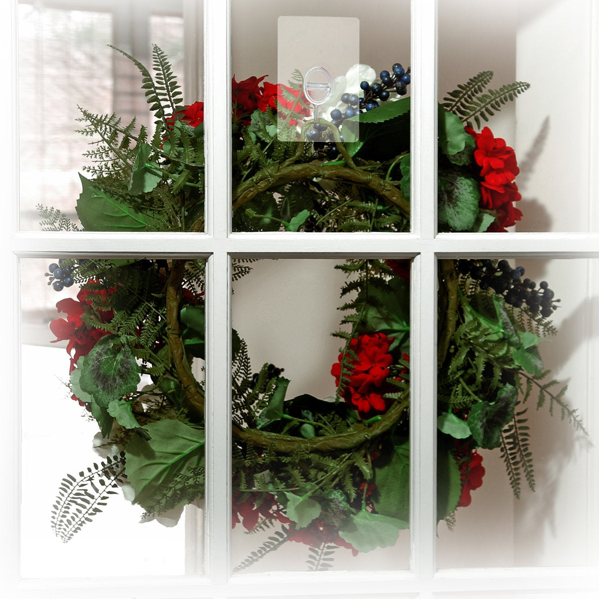 Clear self-adhesive wreath hanger holding a floral wreath on a white multi-pane glass door.