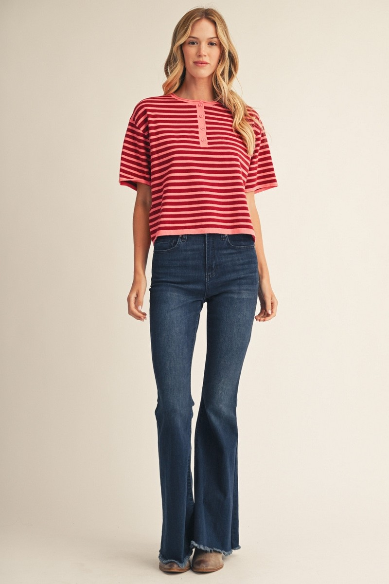 Woman wearing a red and pink striped short-sleeve button-up sweater top with dark flare jeans.